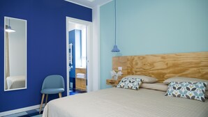 A bedroom with a large bed, a wooden headboard, a blue chair, and a mirror on the wall. - Il Grande Blu (Terracina)