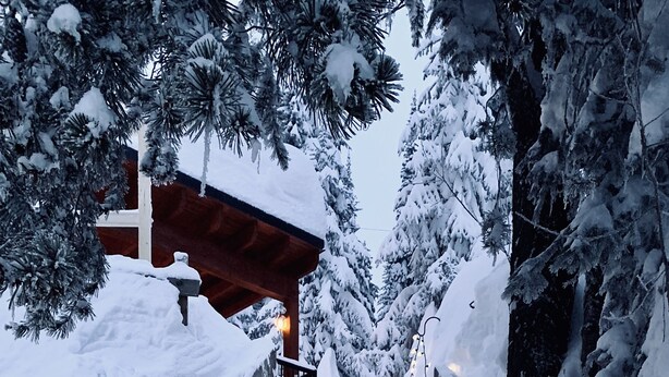 Un escalier recouvert de neige mène à un bâtiment doté d’une balustrade en bois et illuminé de guirlandes lumineuses.