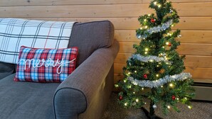Un salon chaleureux avec un canapé gris, un coussin à carreaux et un petit sapin de Noël décoré.