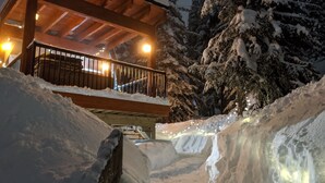 Une cabane en bois dotée d’un balcon, entourée d’arbres couverts de neige et d’un sol enneigé.