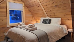 Une chambre confortable dans un chalet en bois, avec un lit, des oreillers et des serviettes soigneusement pliées.