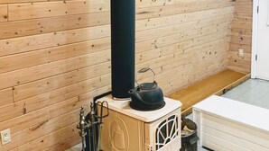 Un intérieur en bois avec un poêle noir, un meuble blanc et un sol carrelé.