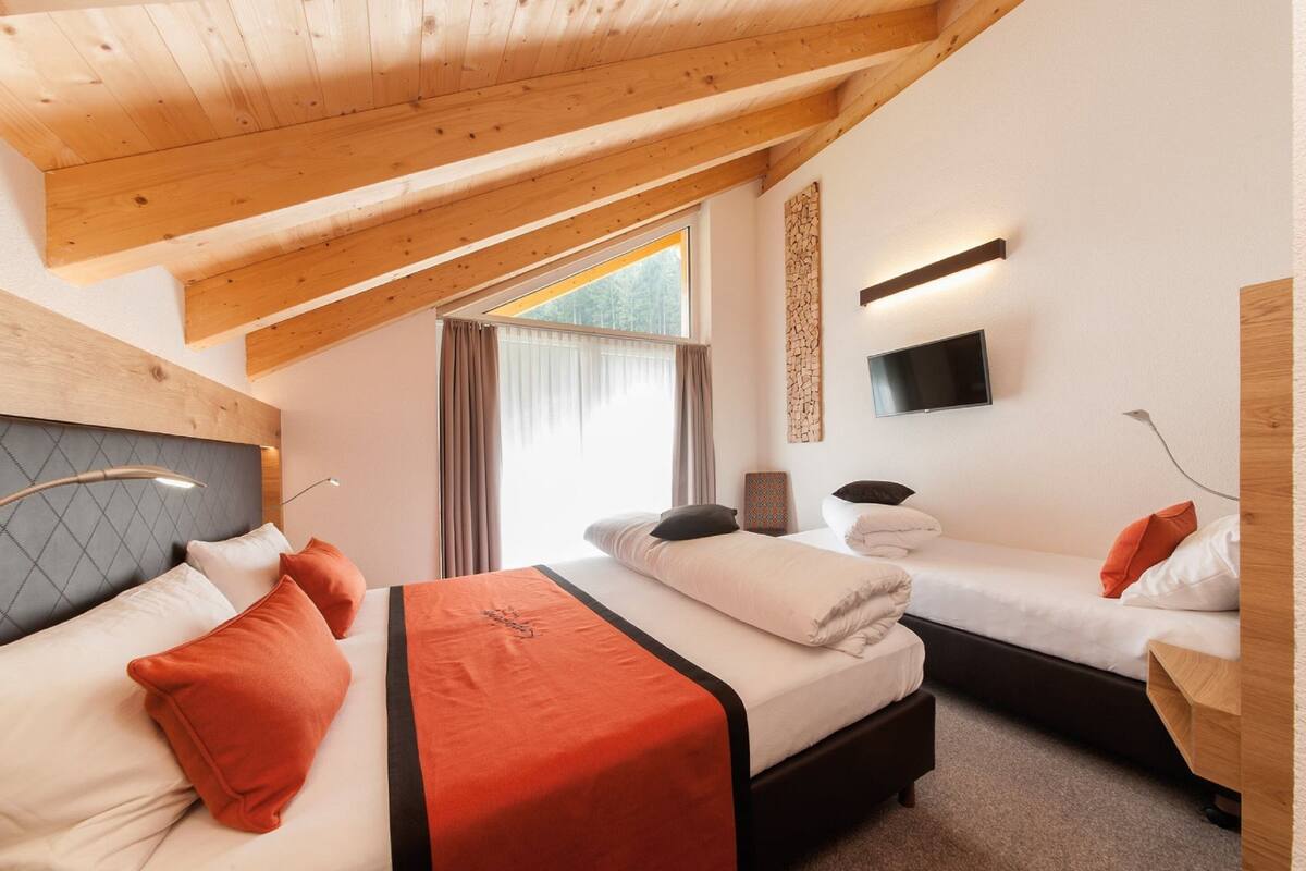 Een moderne hotelkamer met een schuine plafond, twee bedden, een televisie en een groot raam.