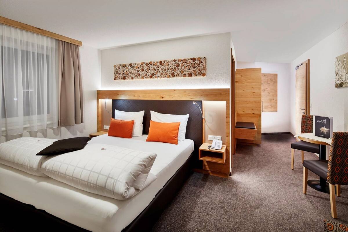 Een hotelkamer met een groot bed, een nachtkastje met telefoon, een stoel en een klein tafeltje met een fotolijst.