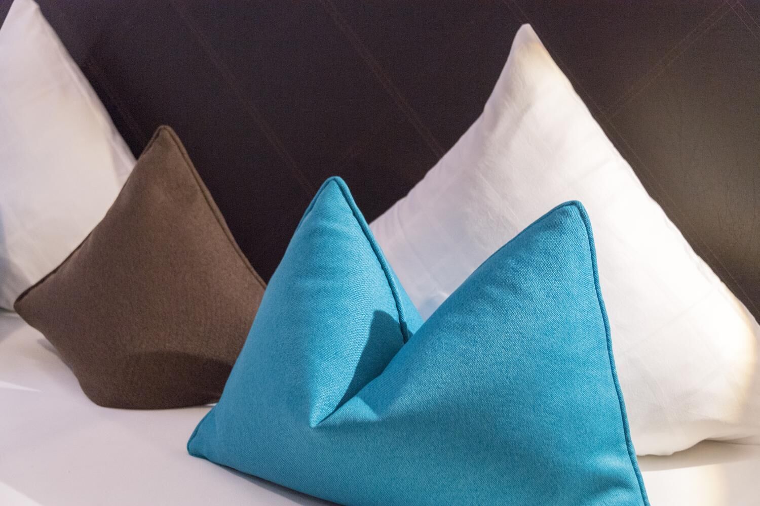 Una cama con tres almohadas de distintos colores.