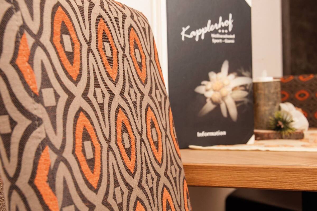 Een patroon stof, een boek met de titel 'Kappelhoff' en een kleine potplant op een houten oppervlak.