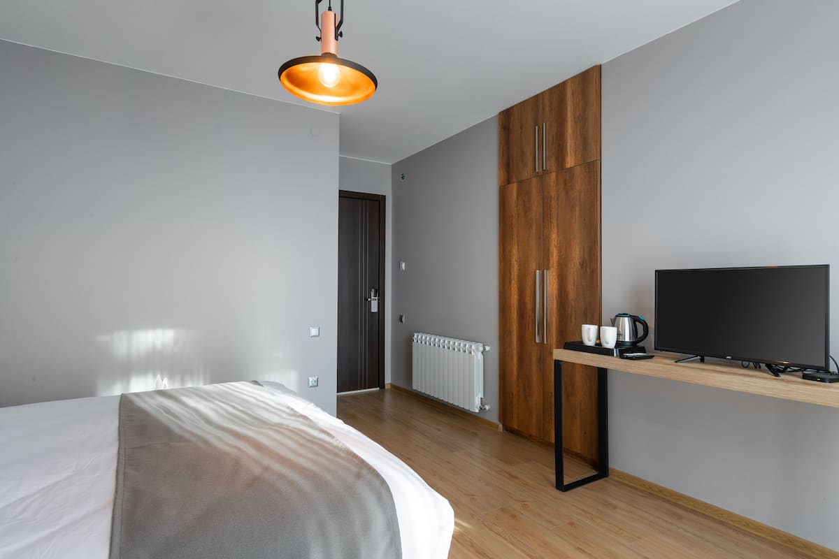 A modern hotel room with a bed, a desk with a flat-screen TV, and a wooden wardrobe.