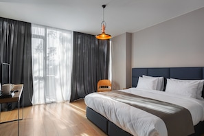 A modern hotel room with a large bed, a desk with a chair, and a view through sheer curtains. - The Berg Hotel (Borjomi)