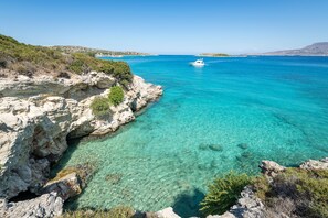 A coastal landscape with clear turquoise waters, rocky cliffs, and a boat in the distance.