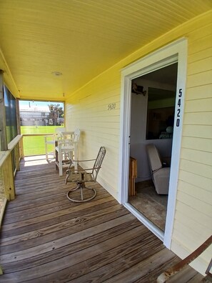A covered porch with a wooden floor, white chairs, and a door leading to an interior space. - Antebellum home with screened front porch and turnaround parking in the rear. (Chauvin)