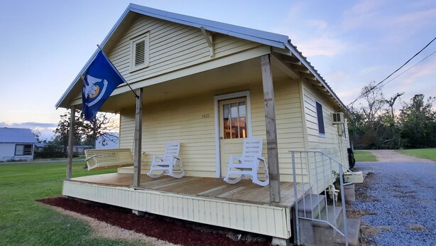 A small, single-story house with a porch, a flag, and a number '5420' on the door. - Antebellum home (Chauvin)