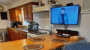 A kitchen with wooden cabinets, a dining table with two chairs, a TV on the wall, and a gas stove. - Antebellum home (Chauvin)