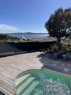 A wooden deck with a swimming pool, lounge chairs, and a view of the sea and distant hills. - Ste-Maxime sea view villa (SAINTE-MAXIME)