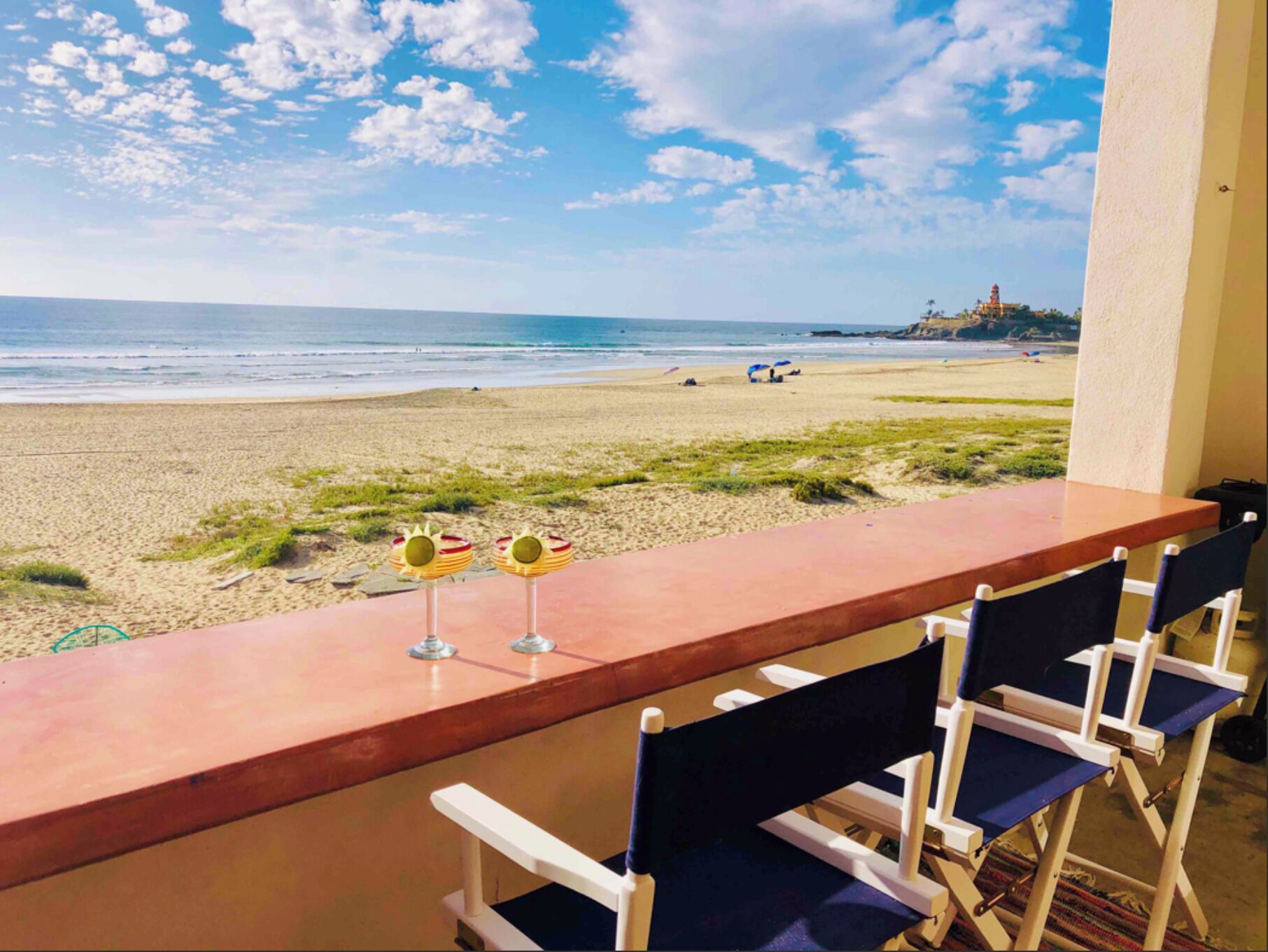 A beach view from a balcony with a wooden table and chairs.