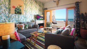 A living room with a couch, armchair, and a colorful rug. There is a television on a stand and a ceiling fan.