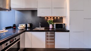 A modern kitchen with white cabinets, a stainless steel range hood, a microwave, and a sink. - Heart of Cannes Amazing design apt Croisette Top Location Olam Properties (Cannes)