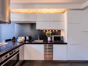 A modern kitchen with white cabinets, a stainless steel range hood, a microwave, and a sink. - Heart of Cannes Amazing design apt Croisette Top Location Olam Properties (Cannes)