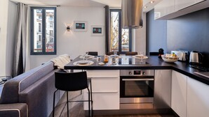 A modern kitchen with a central island, stainless steel appliances, and a dining area with a sofa and chairs. - Heart of Cannes Amazing design apt Croisette Top Location Olam Properties (Cannes)