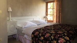 Une chambre à coucher avec un lit, une table de chevet, une fenêtre avec des rideaux et une lampe.