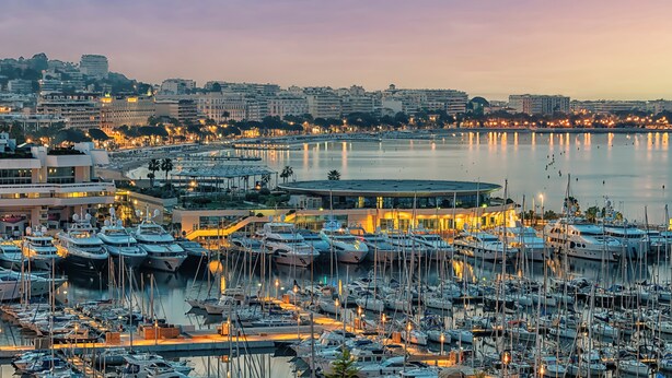 Un port de plaisance où sont amarrés de nombreux bateaux, entouré de bâtiments et bordé d’une promenade au bord de l’eau.