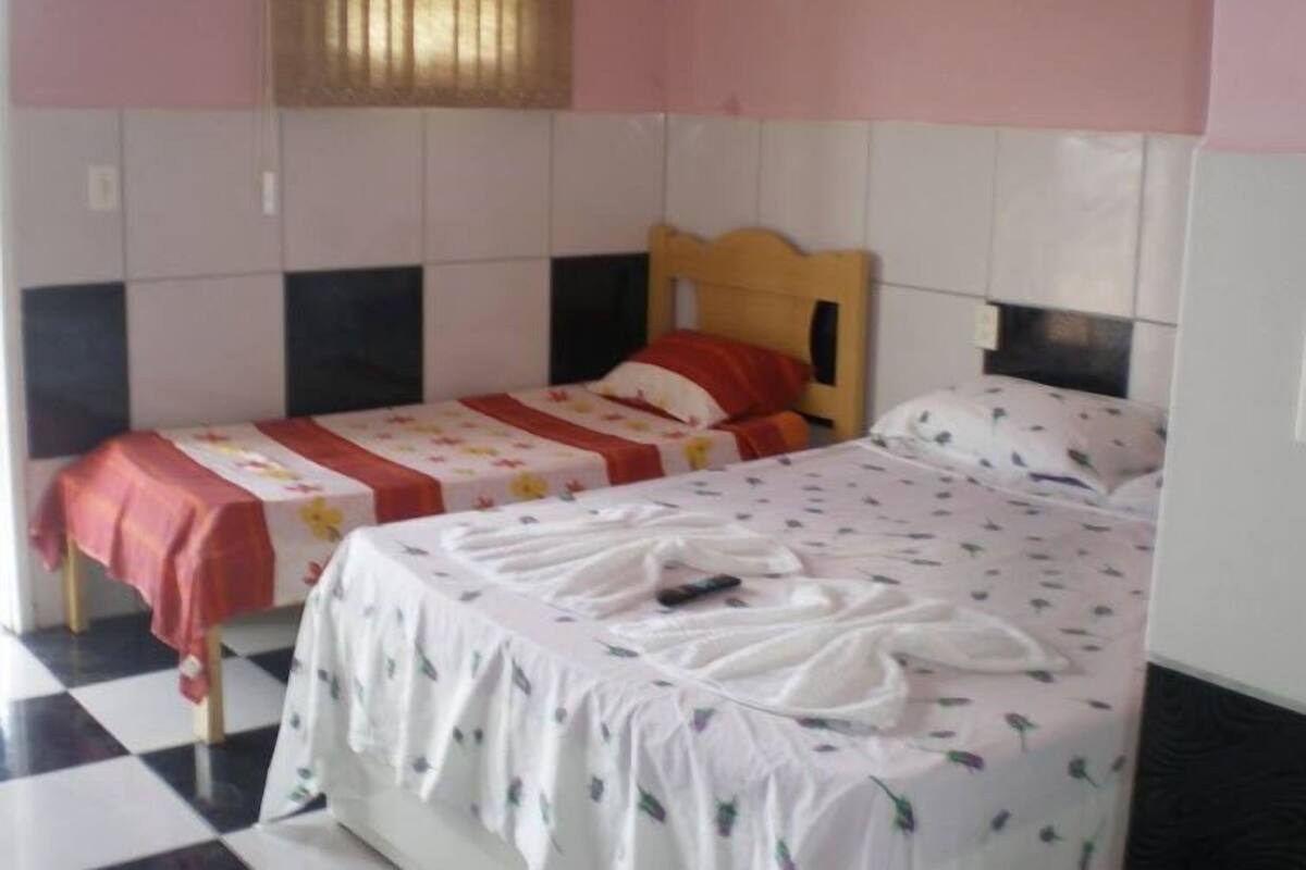 Une chambre avec deux lits, l’un recouvert d’une couvre-lit rouge et blanche, et l’autre d’une couvre-lit blanche à motifs floraux.