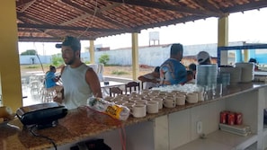 A covered outdoor area with a counter, stacked plates, and a bag of chips. - Pousada Nathymar (Piranhas)