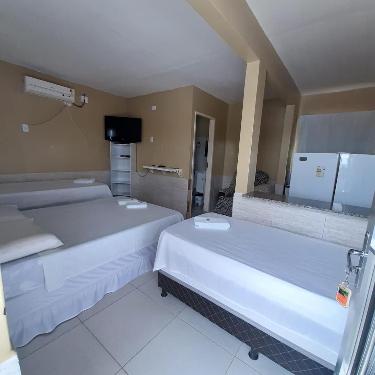 Ein Hotelzimmer mit zwei Betten, einem Fernseher, einem Kühlschrank und einem Fliesenboden.