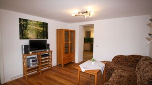 A living room with a wooden floor, a television on a wooden stand, a cabinet, a sofa, and a table with a plant.