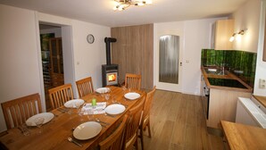 A dining area with a wooden table set for four, a built-in wood stove, and a kitchen with a green backsplash.