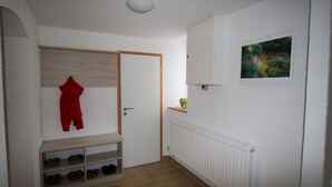 A hallway with a wooden shoe rack, a red garment hanging, a white radiator, and a framed picture on the wall.
