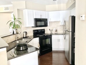 Une cuisine moderne avec des meubles blancs, une cuisinière noire, un four à micro-ondes et un réfrigérateur.