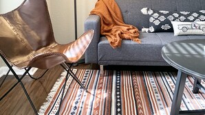 Ein Zimmer mit Ledersessel, grauem Sofa mit Decke, Stehlampe, einem Gemälde mit Pferden und gemusterten Teppichen.