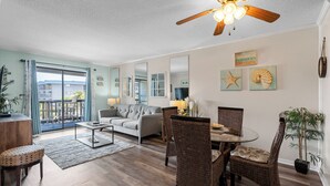 A spacious living room with a grey sofa, wicker chairs, a glass coffee table, and a ceiling fan.