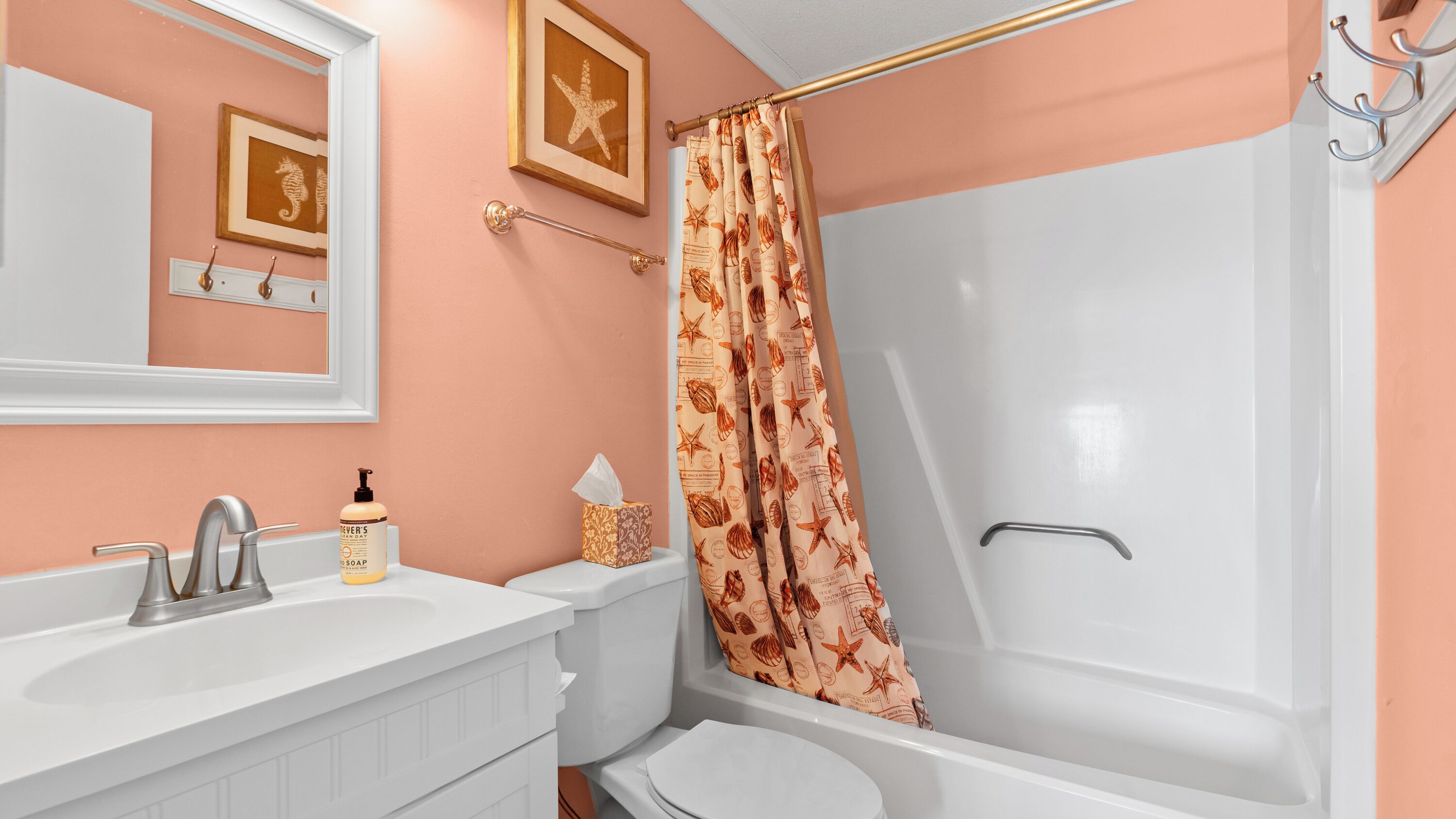 Ein Badezimmer mit weißem Waschbecken, Toilette und Badewanne. Über dem Waschbecken hängt ein gerahmtes Bild, und an einem Handtuchhalter hängt ein Handtuch.