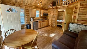 A log cabin interior with a dining area, kitchen, and seating space. - Secluded Creekside Cabin (Coaldale)