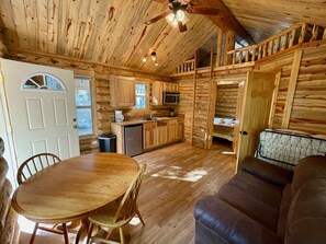 Cozy cabin-style interior with a dining table, sofa, and bench, plus a kitchenette with microwave and sink.
