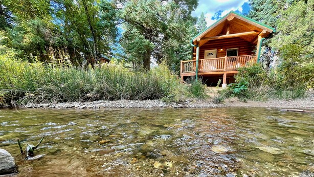 A wooden cabin with a balcony overlooking a clear stream. - Secluded Creekside Cabin (Coaldale)