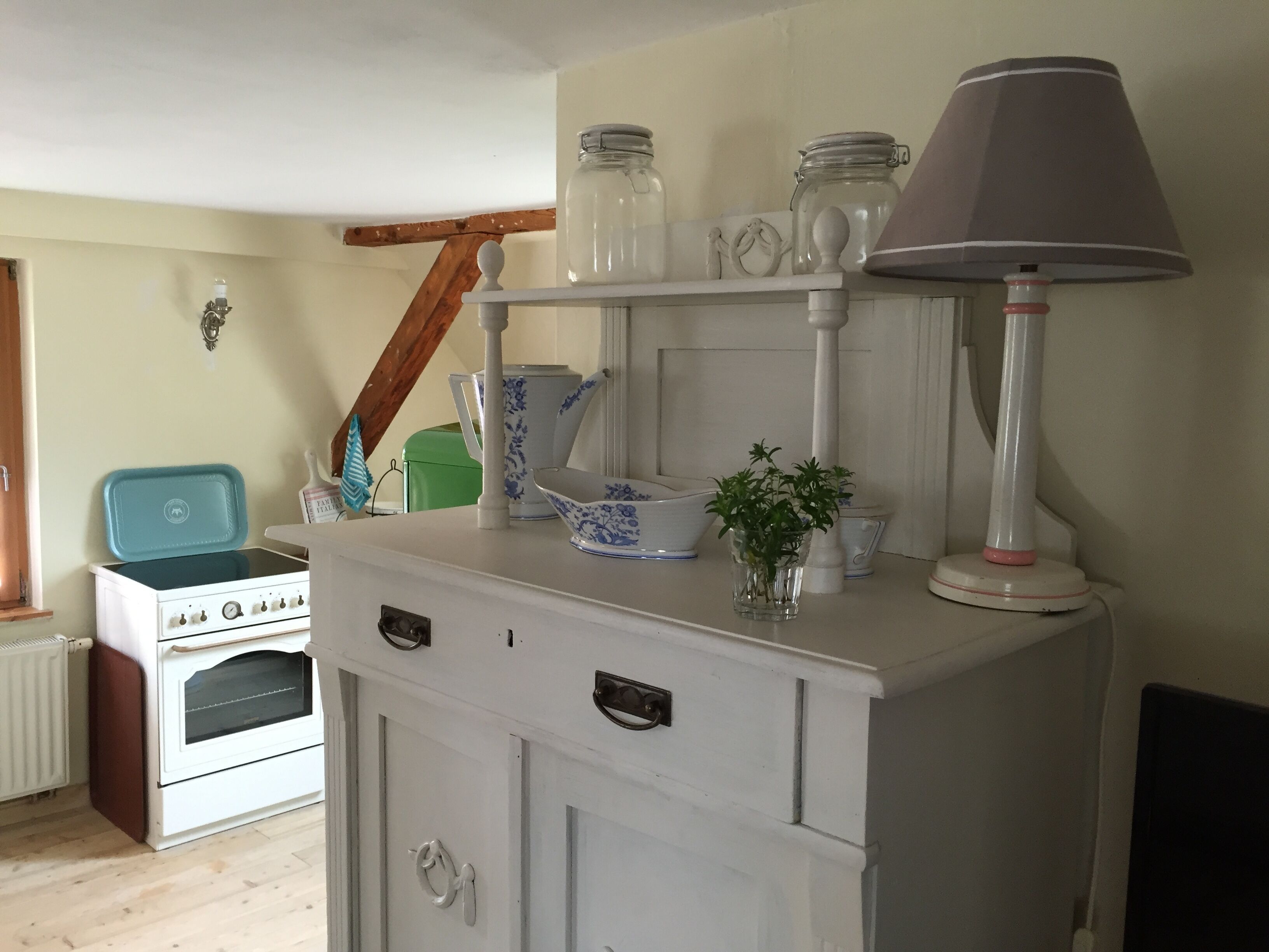 Une cuisine avec un four blanc, un meuble blanc doté de tiroirs, une petite plante posée sur le comptoir et une lampe sur le dessus.