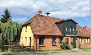 A two-story building with a red-tiled roof, a brick facade, and a green door.