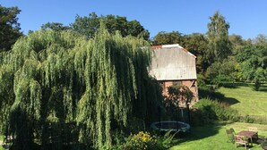 A rustic building with a metal roof, surrounded by lush greenery and a small trampoline. - Apartment Ida up to 6 people (Stuer)