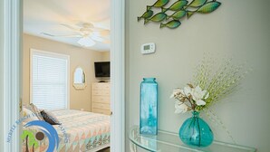 Ein Schlafzimmer mit Bett, Deckenventilator, Fernseher, Kommode, einer Blumenvase und einer Wanddekoration.