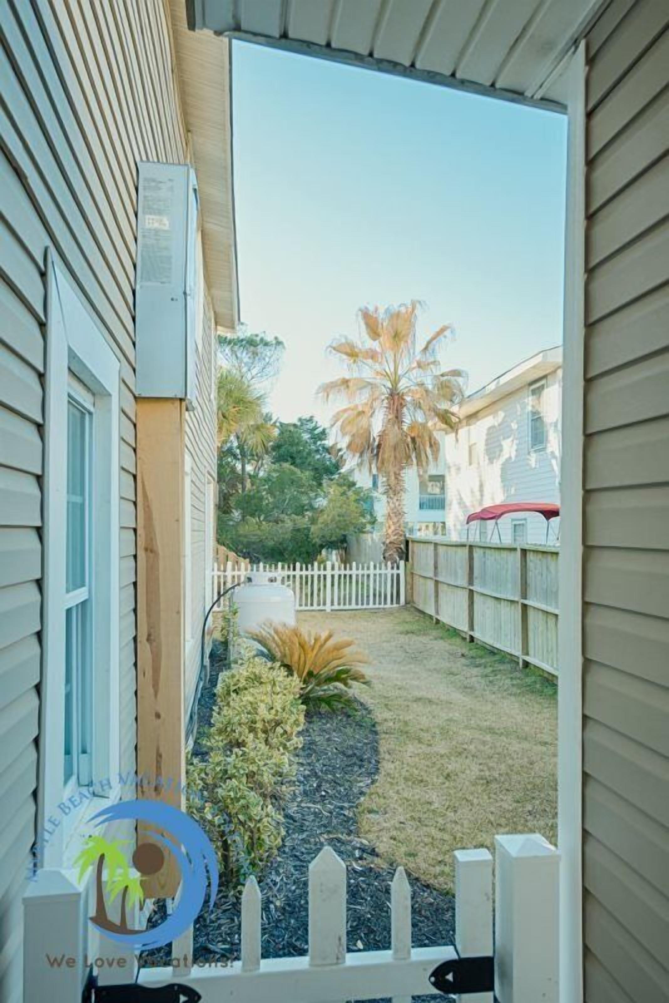 A view of a backyard with a palm tree, a white picket fence, and a small garden area.