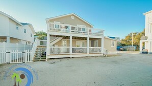 Maison de vacances en bord de mer, sur deux étages, avec balcon, allée privée clôturée et vue sur un ciel dégagé.