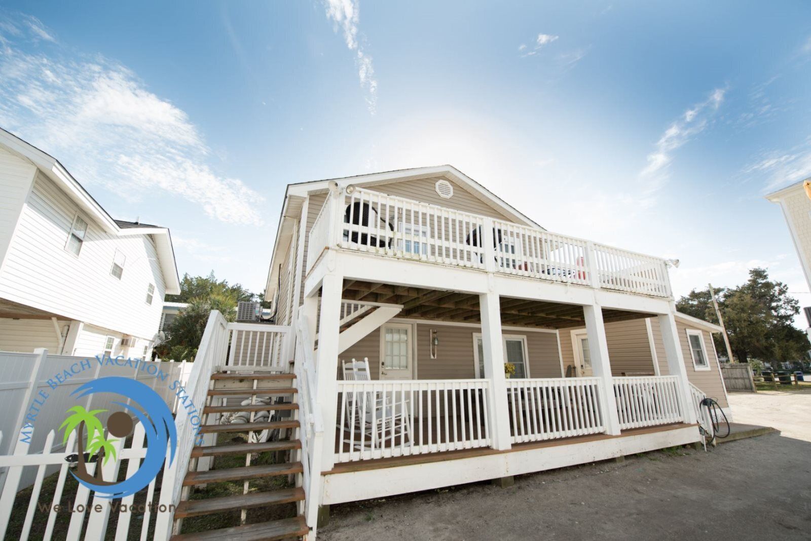 Ein Strandhaus mit zwei Etagen, einem Balkon und einer Veranda.