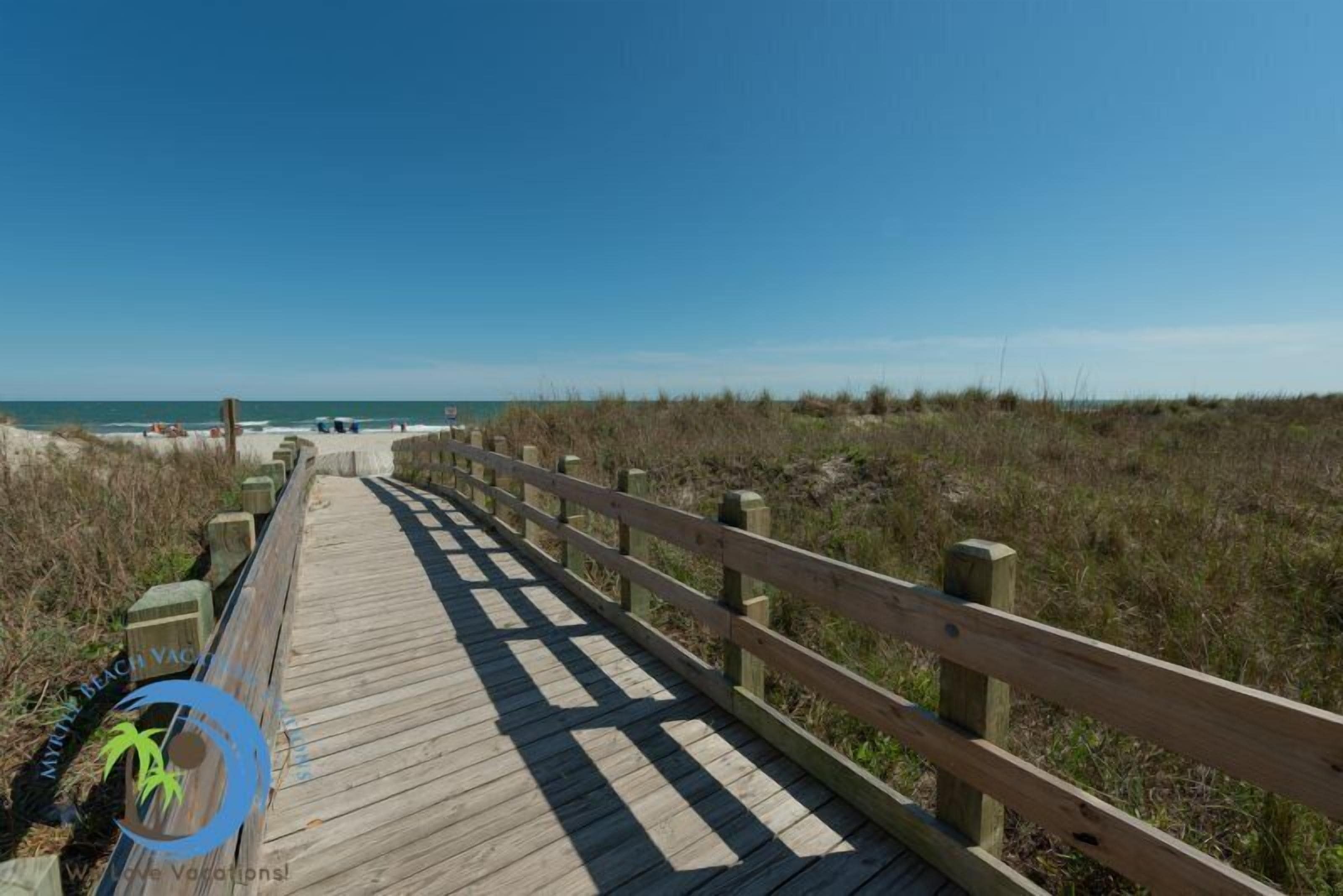 A wooden boardwalk leading to a beach with clear skies.