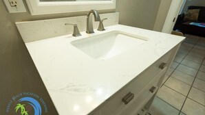 A bathroom with a white sink, two faucets, and a window above the sink.