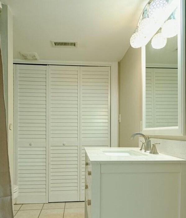 Un baño con un tocador blanco, un lavamanos y un espejo con iluminación. Se ve una puerta blanca al fondo.