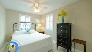 A bedroom with a bed, a dresser, a nightstand, a lamp, a ceiling fan, and a window.