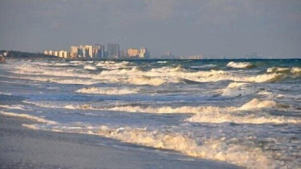 A beach with waves and a distant city skyline.