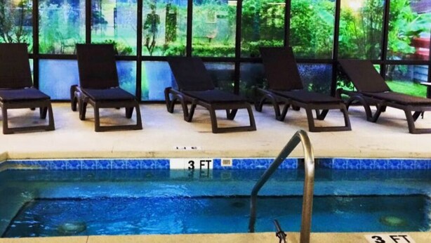 An indoor swimming pool with a 3 FT depth marker, surrounded by lounge chairs and large windows offering a view of greenery. - CG Efficiency (North Myrtle Beach)